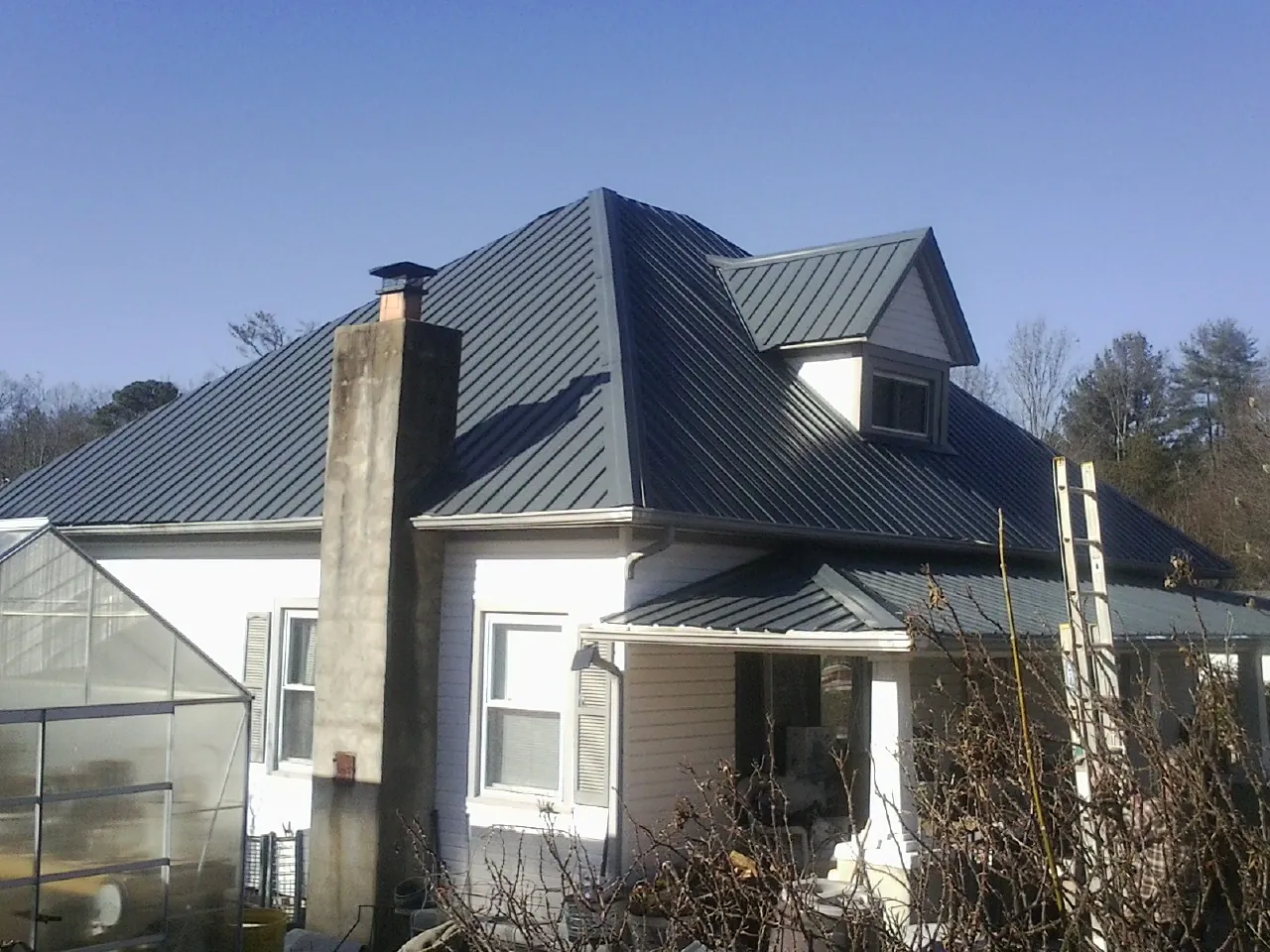 Dark blue standing seam metal roof on a white farmhouse with dormer — Slate & Tile Roof Repair by Roofing Brothers in Conway Springs