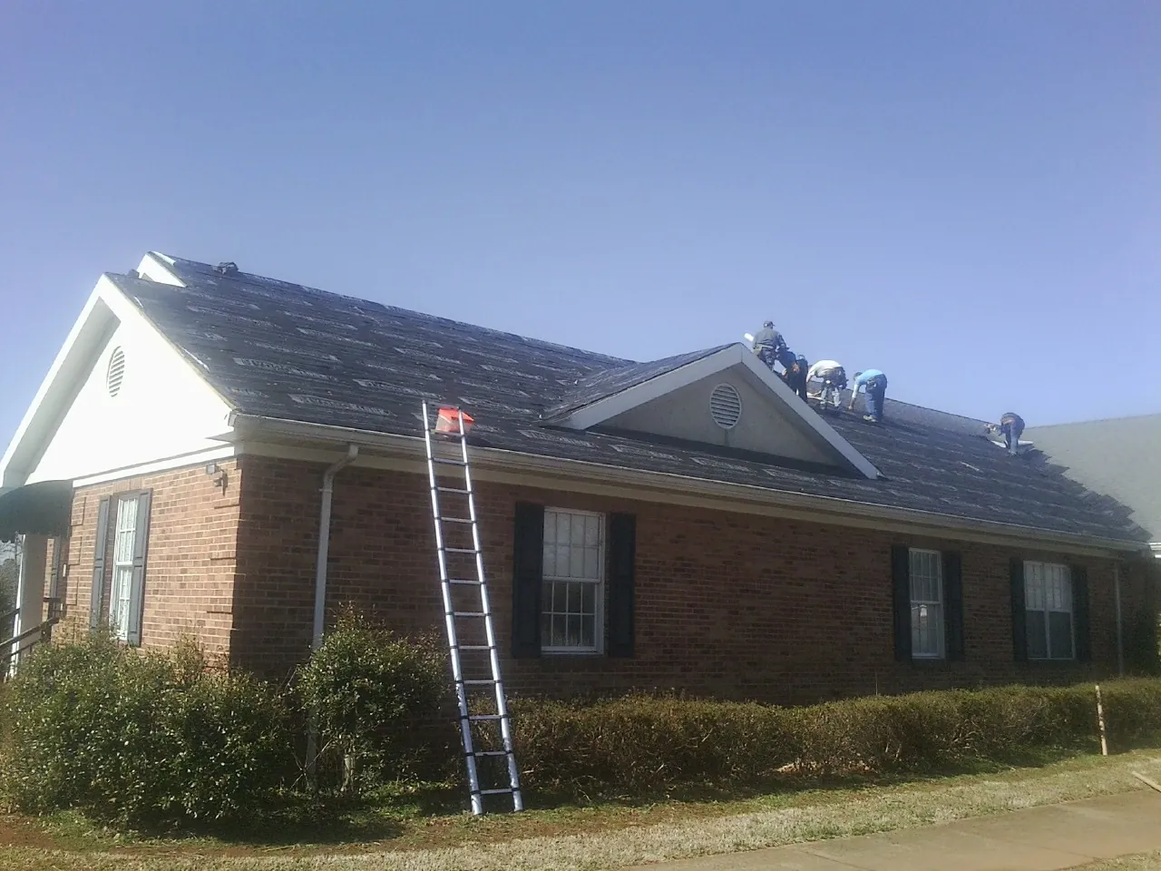 Crew tearing shingles off a brick ranch roof with a ladder set — Emergency Roof Repair work by our crew in Conway Springs