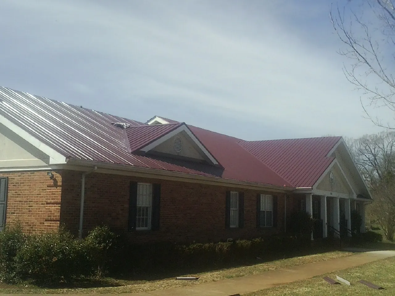 Red metal roof with gabled entries on a long brick building, from a Hail Damage Roof Repair job in Conway Springs
