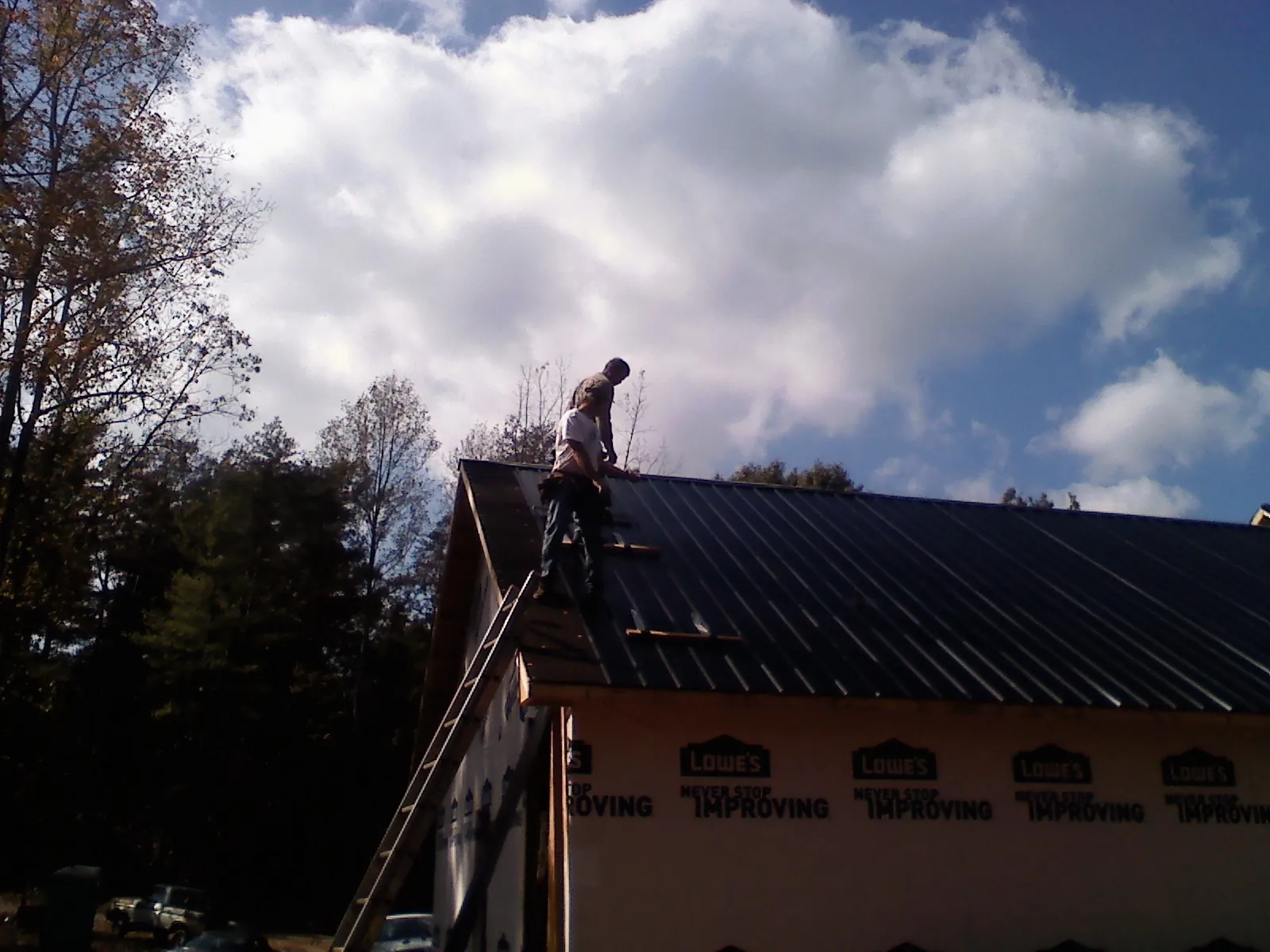 Roofer fastening dark metal panels high against a cloudy sky, from a Roof Inspection job in Conway Springs