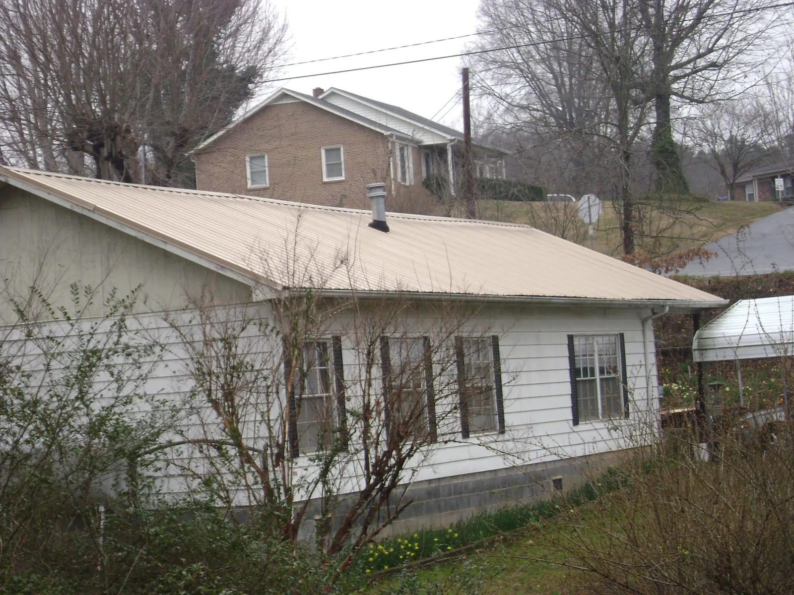 Tan metal roof on a white sided house set into a hillside — Commercial Roofing by Roofing Brothers in Conway Springs