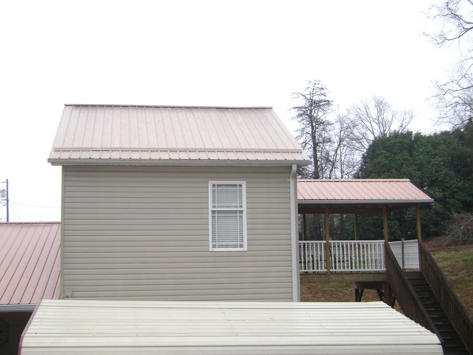Tan metal roofs on a two story addition and attached porch, from a Roof Replacement job in Conway Springs